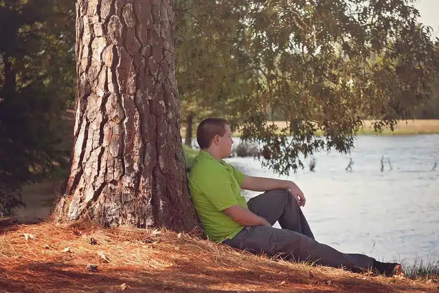 A kid sitting on a tree looking out at a lake