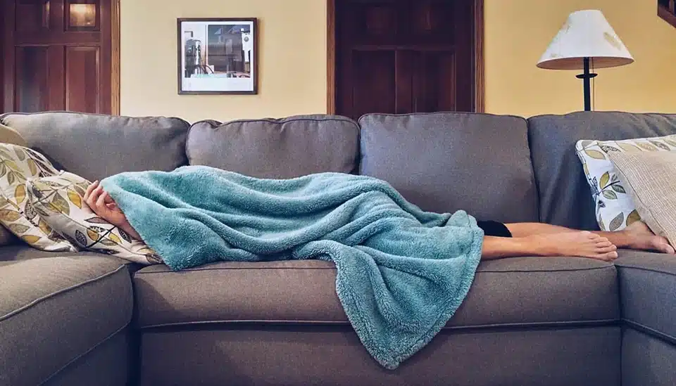 Person laying on couch covered in a blanket