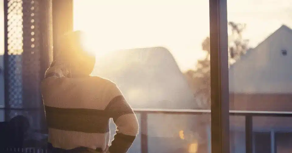 Person looking out a window at a sunset