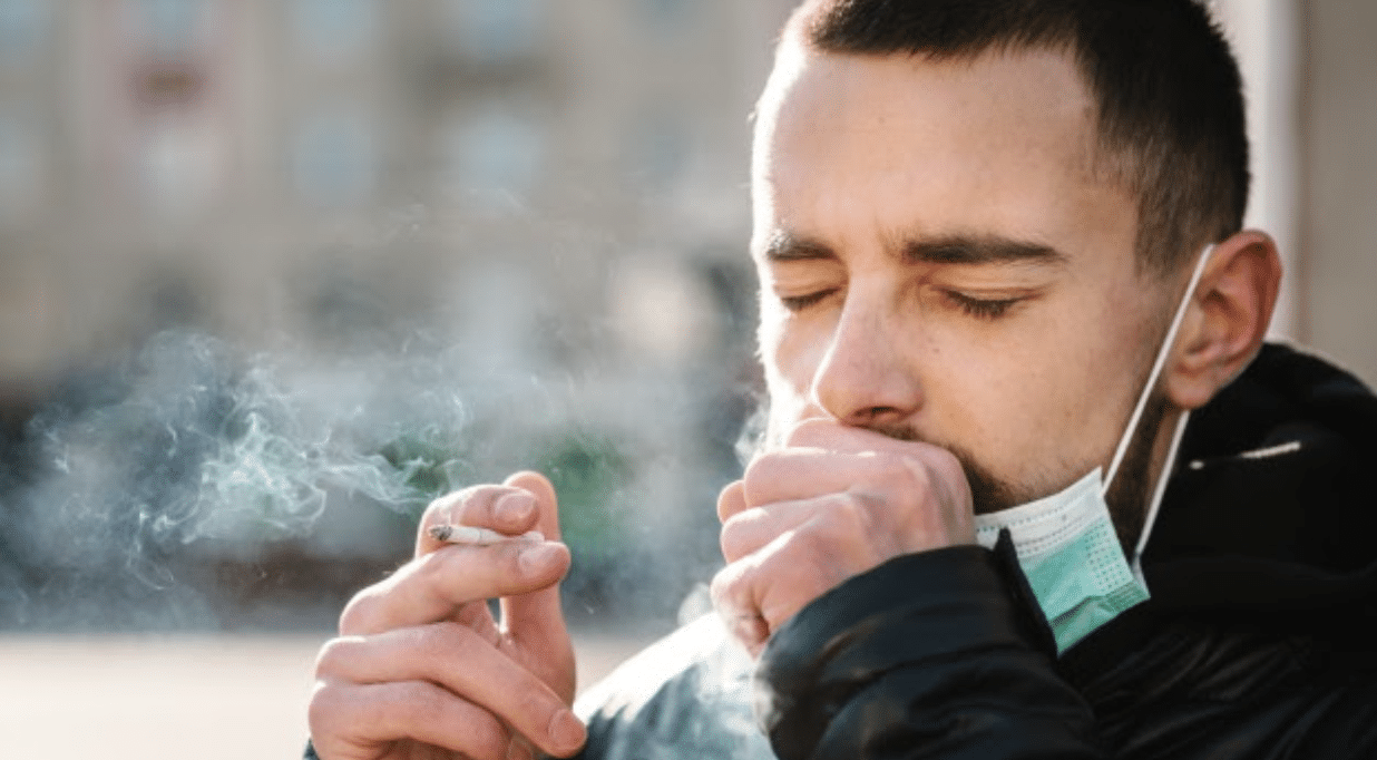 man coughing with cigarette in hand