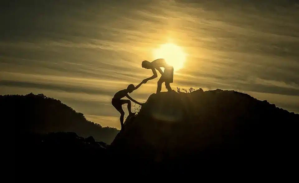 Person helping another one climb up a mountain