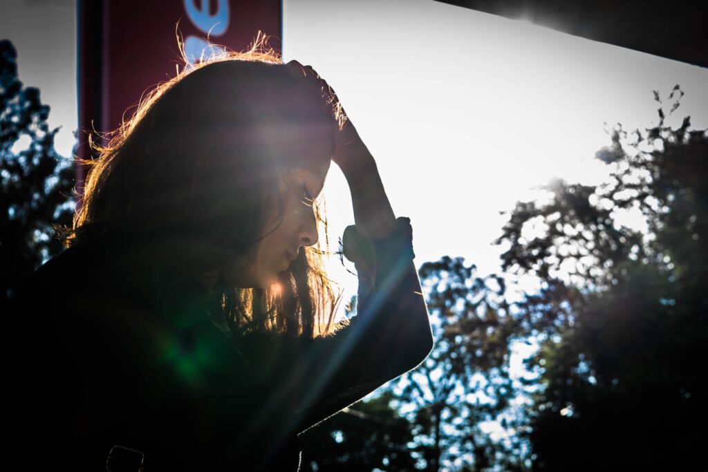 A photo of a person sitting in the sun, holding their head in their hands.
