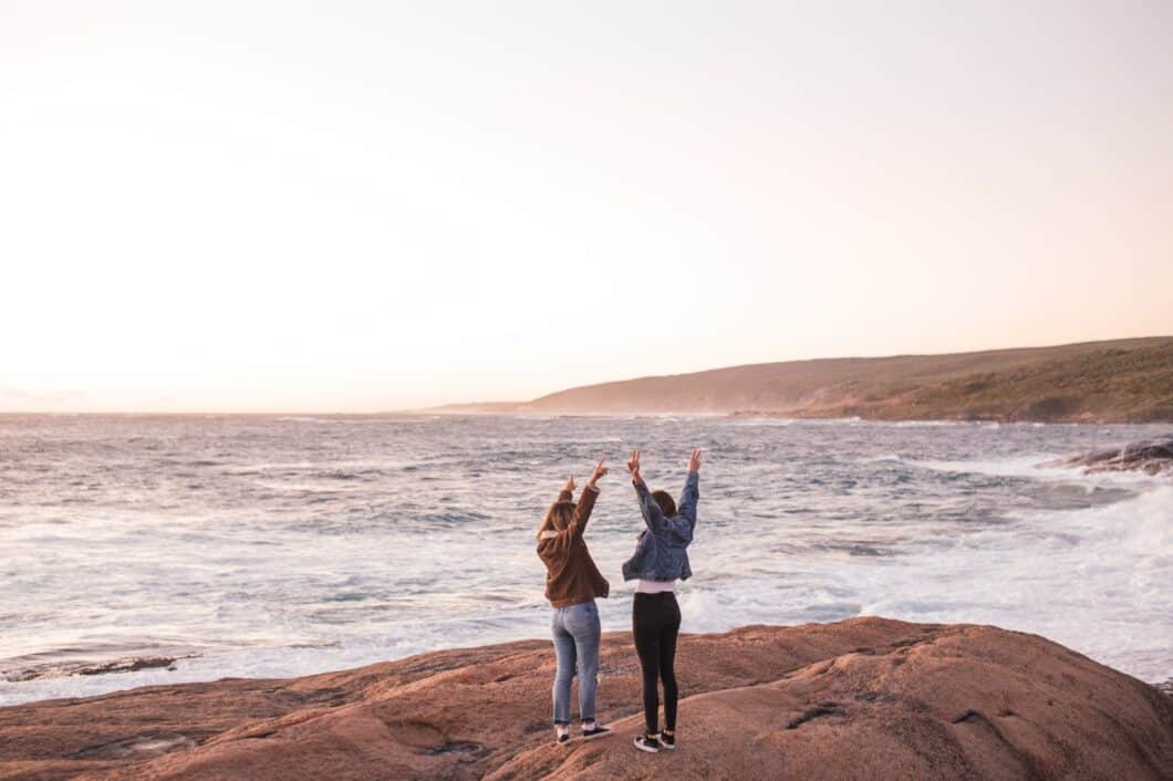 A photo of two people standing in front of the ocean, holding hands and raising their arms in the air. Located near Opus Health