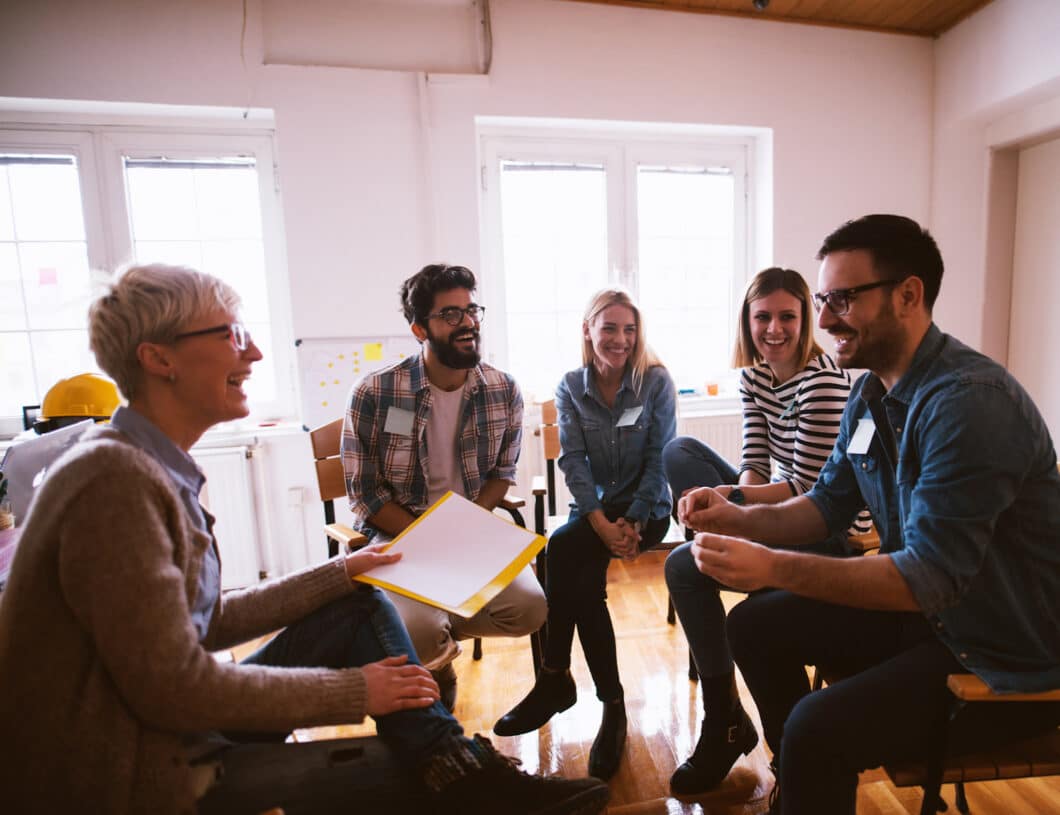 A photo of a group of people in group therapy, smiling and talking.-Support Groups Can Make a Difference in Addiction Recovery. Group of People in Group Therapy Feeling Positive.