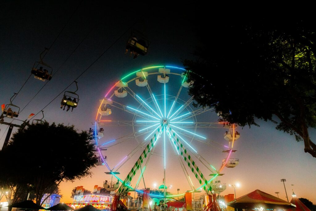 Costa Mesa Fair at night: Ferris wheel and sky ride illuminated with colorful lights.