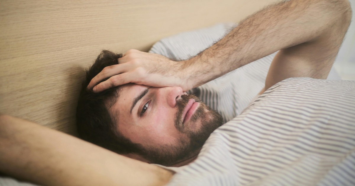 Man experiencing cocaine comedown symptoms, lying in bed with a headache. Focus on managing withdrawal and recovery.