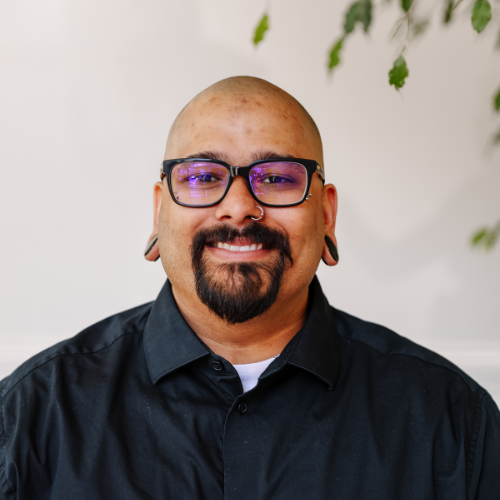 Our Team: Portrait of Julian Primm, smiling man with glasses, beard, and nose ring, team member profile.