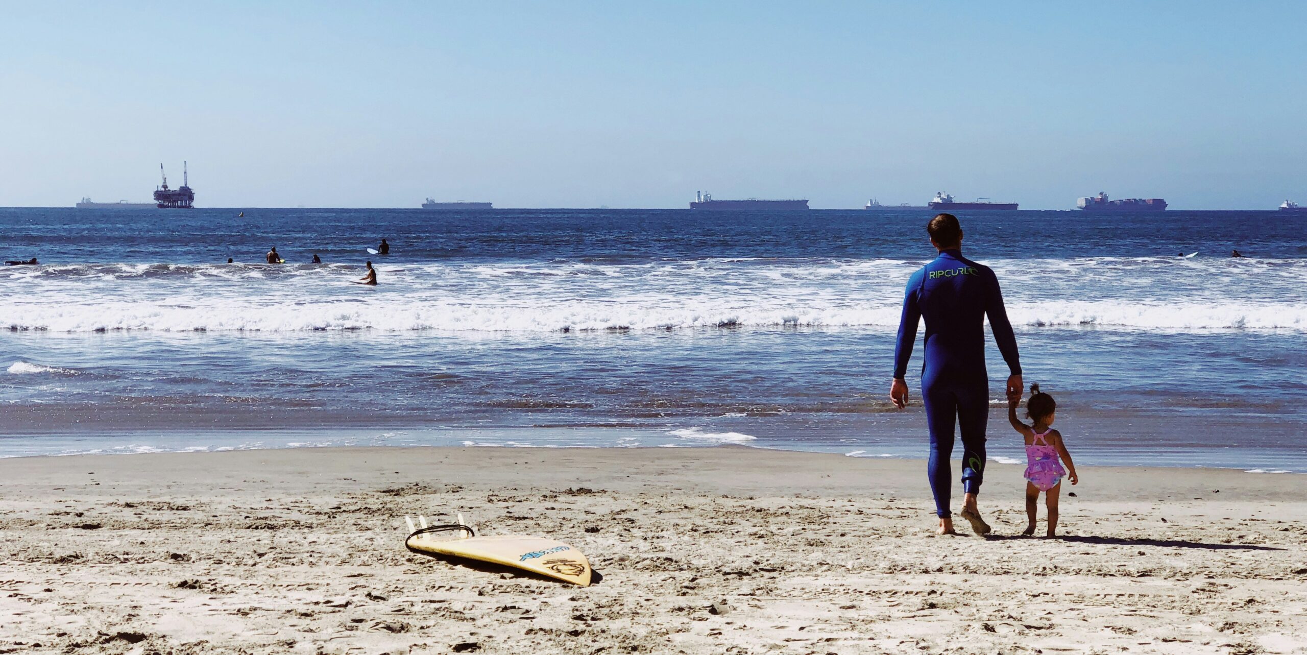 Man and young girl walking the shoreline of Seal Beach, CA.