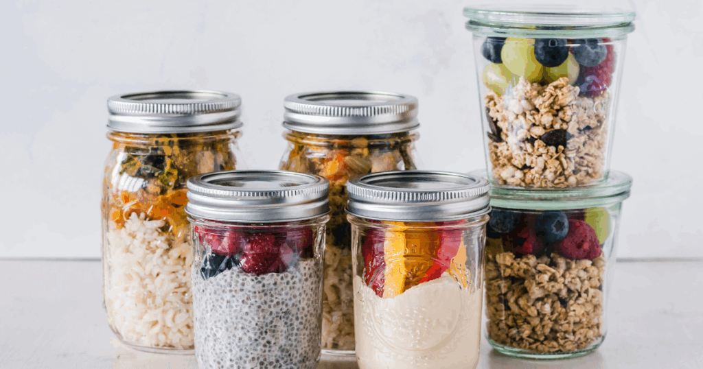Mason jars with healthy breakfast: overnight oats, chia pudding, granola and berries. Meal prep for easier transition.