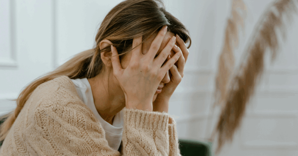 Woman experiencing Wellbutrin withdrawal symptoms, covering face in distress. Side effects and coping with medication withdrawal.