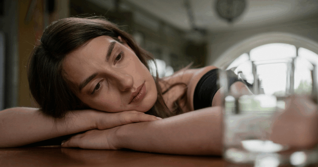Woman experiencing Suboxone withdrawal symptoms, resting head with a glass of water. Focus on opioid recovery and duration.