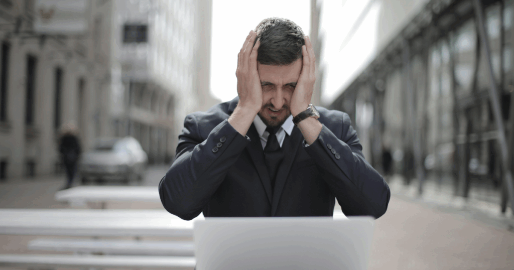 Sertraline Withdrawal: Stressed businessman with head in hands in front of laptop, experiencing withdrawal symptoms.