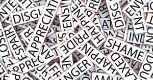 Chaotic pile of sign cards bearing blunt words like 'DISGUST' and 'SHAME', illustrating social stigma and labeling.