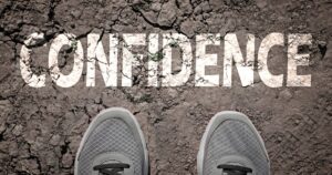 Cracked earth with the word CONFIDENCE and gray sneakers in the foreground.