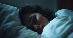 Person sleeping peacefully in a bed with a white blanket in a dimly lit room.