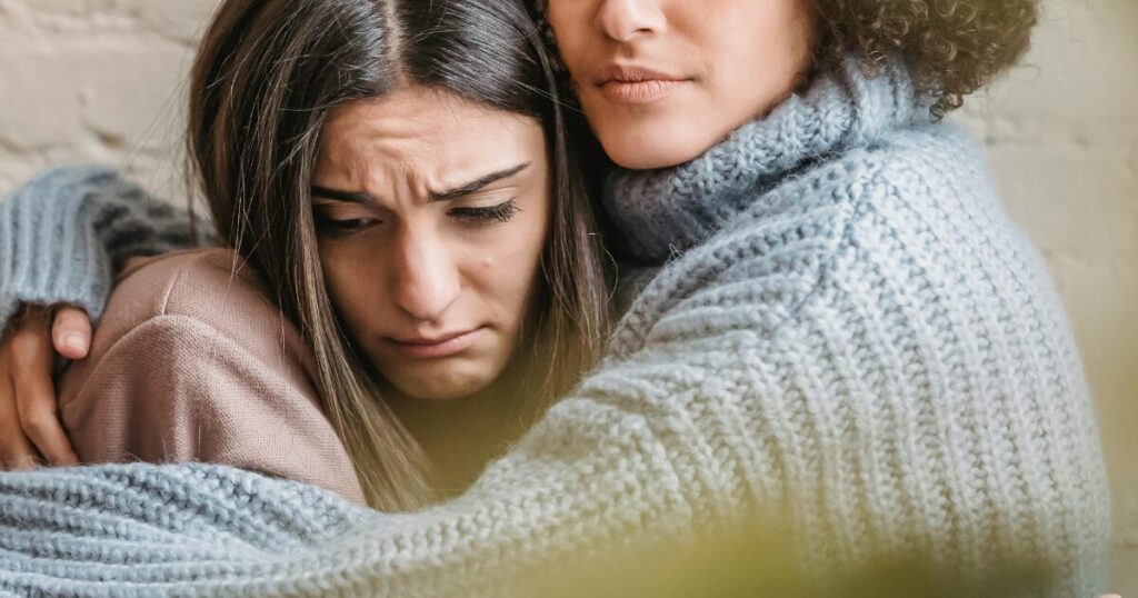 image - Opus Health Two people share a reassuring hug; one appears sad with a frown and furrowed brows.