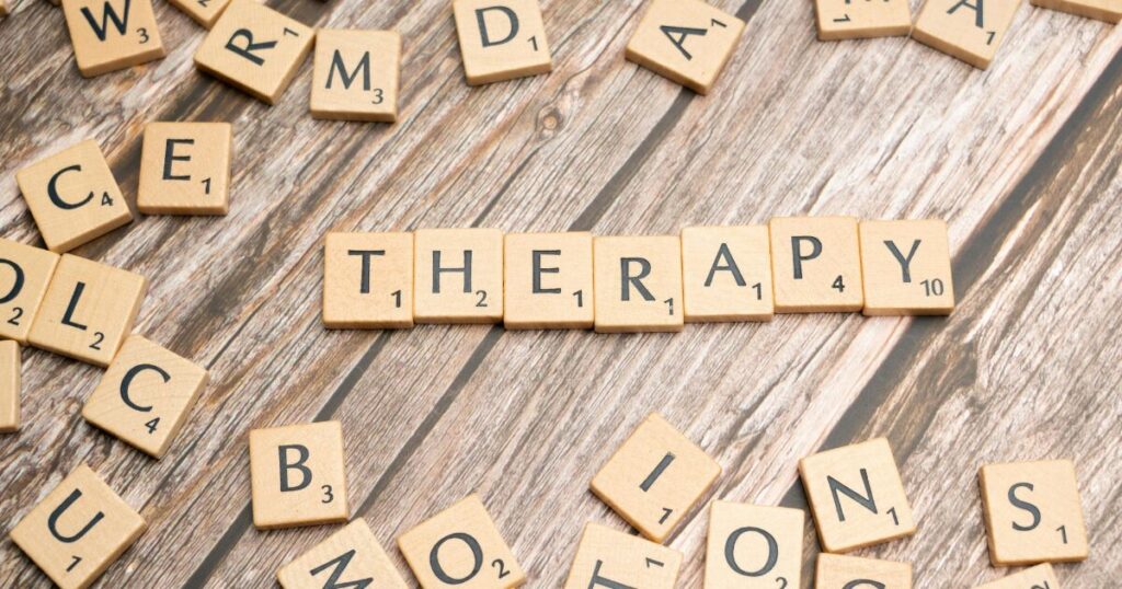 image - Opus Health Tiles spell the word THERAPY on a wooden table, with many scattered Scrabble tiles around it.