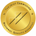 Gold circular accreditation seal reading 'The Joint Commission National Quality Accreditation' along the rim with two stars on either side; abstract interlocking squares and diagonal lines in the center.