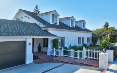 Santa Ana home exterior: White house with dormers, gray roof, black garage door, and white picket fence. Well-maintained property.