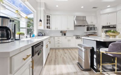 Bright, modern kitchen with white cabinets, marble countertops, stainless steel appliances, and a large window.