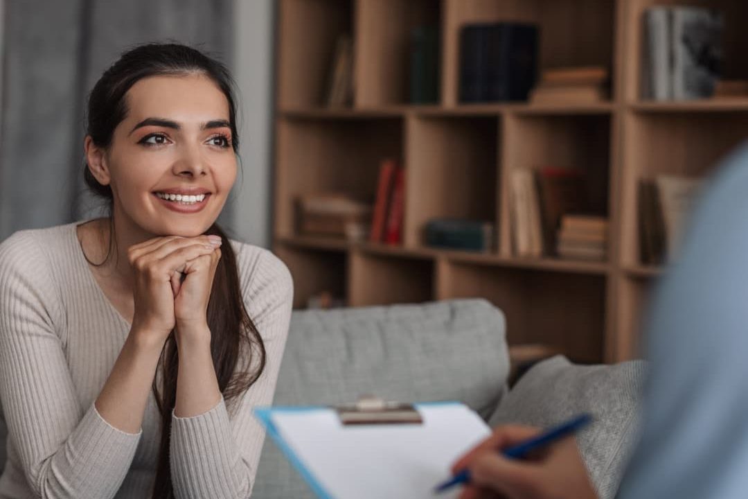 Smiling woman in therapy session discussing treatment options with therapist taking notes.