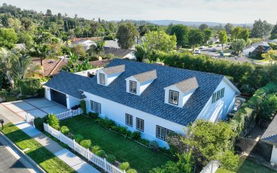 Santa Ana home with new roof. Aerial view of white house with blue roof, dormers, and white picket fence. Landscaped property.