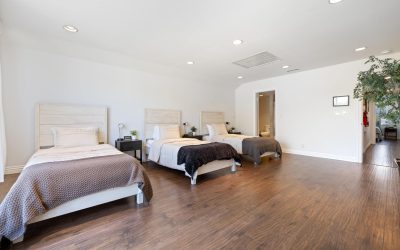 Spacious bedroom interior with three single beds, minimalist decor, hardwood floors. Ideal for group lodging, Santa Ana treatment center.