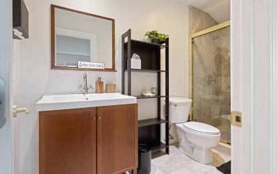 Bathroom interior with wood vanity, sink, mirror, shelving unit, toilet, and shower. Modern bathroom design.