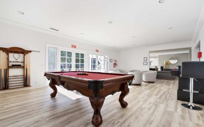 Bright game room featuring a wooden pool table with red felt and ornate legs, plus modern seating and light wood floors.