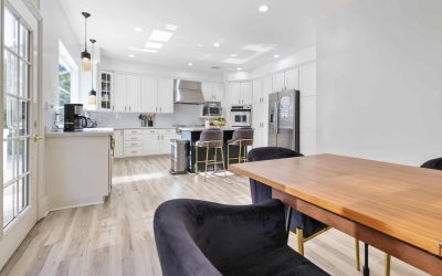 Bright kitchen design with white cabinets, stainless steel appliances, island with seating, and wood dining table. Modern kitchen.
