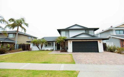 Tour our LP facilities: Exterior view of a two-story house with a black garage door, palm trees, and green lawn.