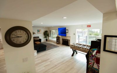 Tour our facilities: View of the CariHouse living room featuring a foosball table, TV, and comfortable seating area near the pool.