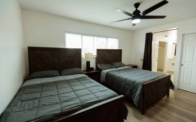 Cari House bedroom with two beds, ceiling fan, and ensuite bathroom. Tour our accessible facilities now.