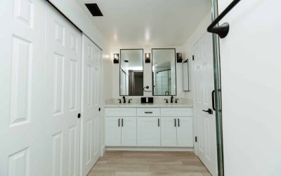CariHouse bathroom facility tour: Modern white double vanity with black fixtures and mirrors, contrasting with light wood flooring.