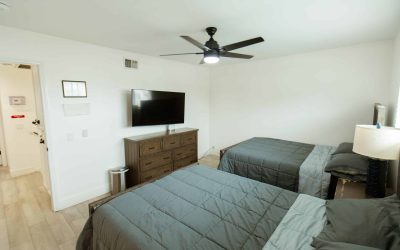 LP Facilities tour: Bedroom with two beds, TV, ceiling fan. CariHouse interior showcasing modern living space.