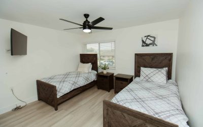 Cari House bedroom facility tour, featuring two beds, nightstands, and a ceiling fan providing a comfortable living space.