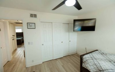 LP Facility Tour: Bright room with white closet, TV, ceiling fan, and bed, showcasing a comfortable living space.
