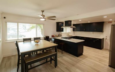 Cari House kitchen and dining area featuring dark cabinetry, island, seating, and modern appliances for a comfortable living space.