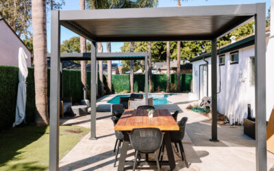 Outdoor living space with modern pergola over a dining table, pool and greenery in the background. Backyard patio design.