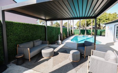 Outdoor living space with modern pergola, gray sofa, chairs, and pool. Backyard patio design with sleek furniture.