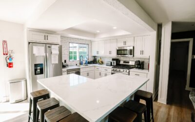 Bright, modern kitchen with white cabinets, marble countertops, and stylish stools at the island. Stainless steel appliances.