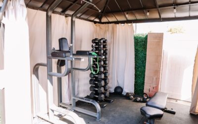 Home gym setup with weight rack, pull-up station, adjustable bench, kettlebells, and medicine ball in covered outdoor space.
