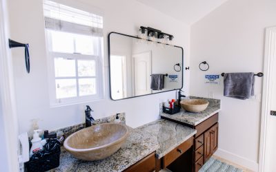 Modern bathroom with double granite vanity, vessel sinks, black fixtures, and large mirror reflecting a bright, clean space.