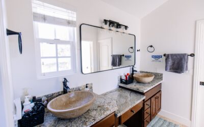 Modern bathroom with double granite vanity, vessel sinks, black fixtures, and large mirror reflecting a bright, clean space.