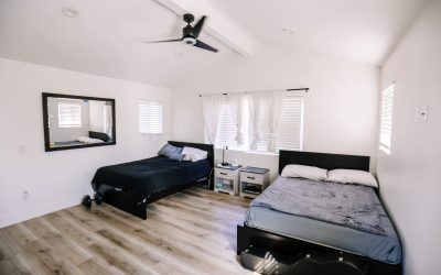 Bright bedroom with two beds, wood floors, ceiling fan, and a large mirror. Modern bedroom interior design.