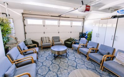 Garage conversion design with seating area, modern gray chairs, round coffee table, and blue patterned rug for a cozy space.