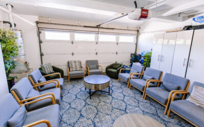 Garage conversion design with seating area, modern gray chairs, round coffee table, and blue patterned rug for a cozy space.